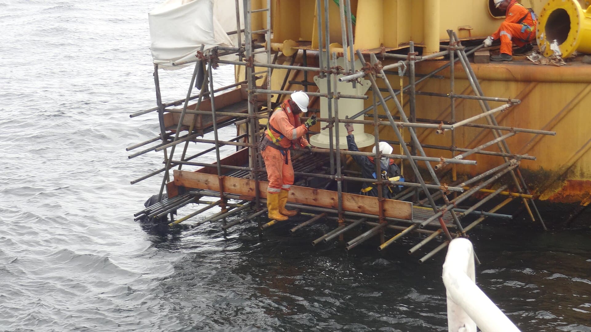 Offshore crew in coveralls working on scaffolding beside a platform leg